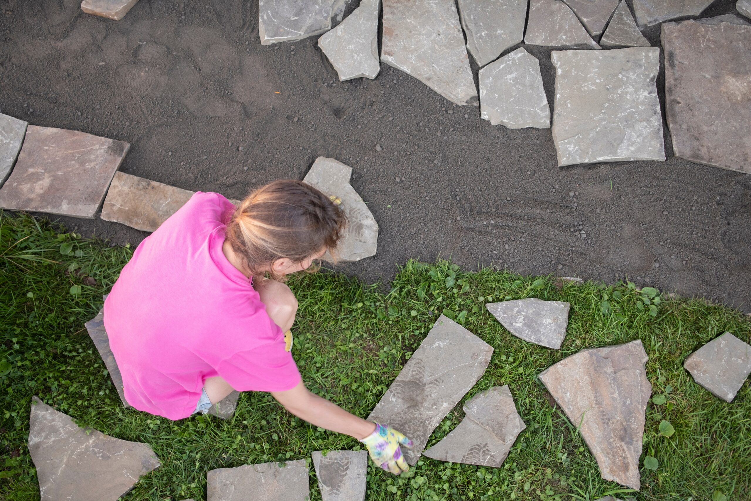 a woman laying stone paving slabs outdoors as a DIY backyard project