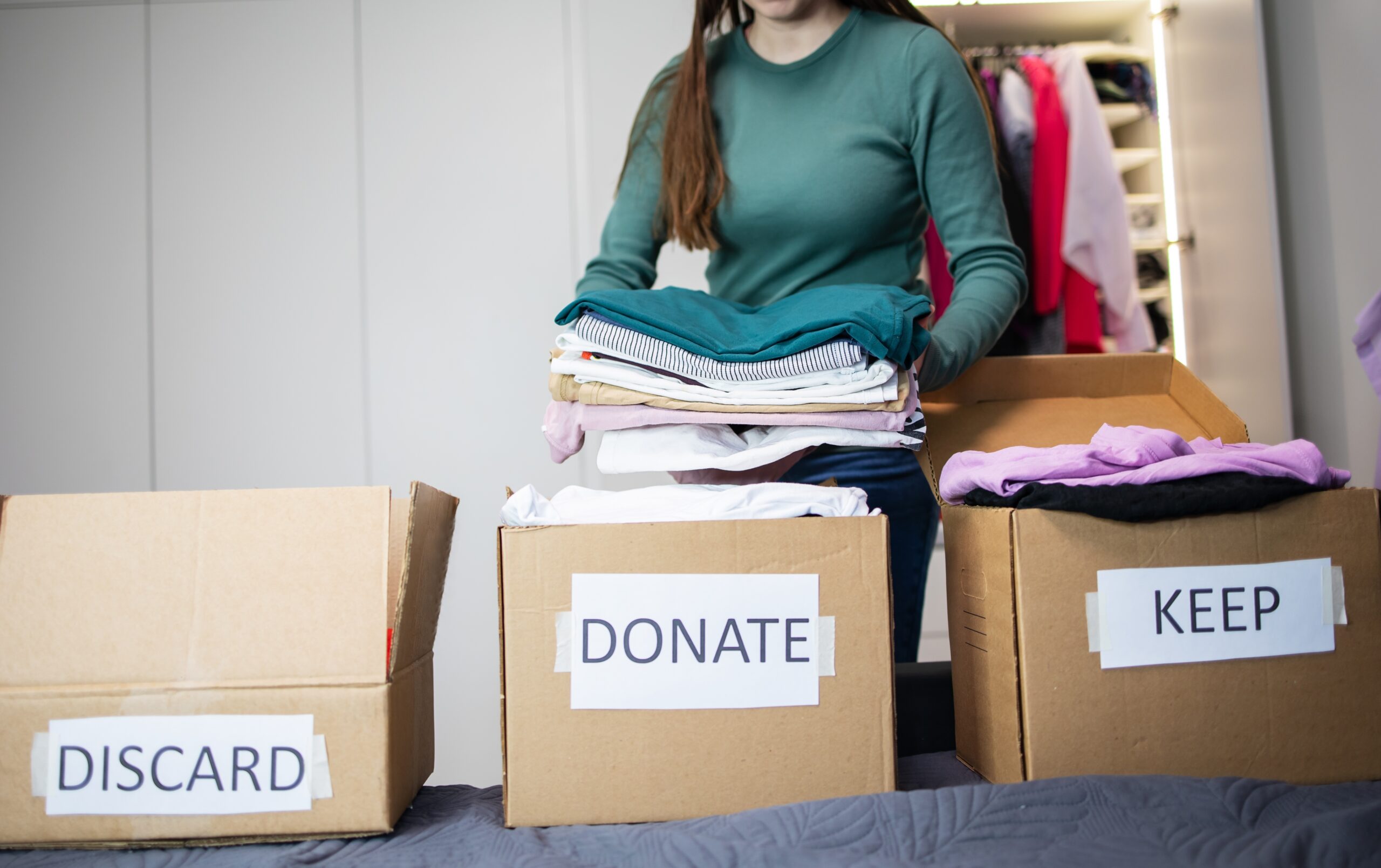A woman sorting clothes into 3 boxes: Keep, donate, and discard