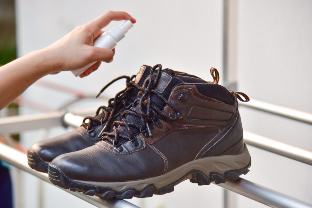 a hand spraying cleaner to a pair of hiking boots